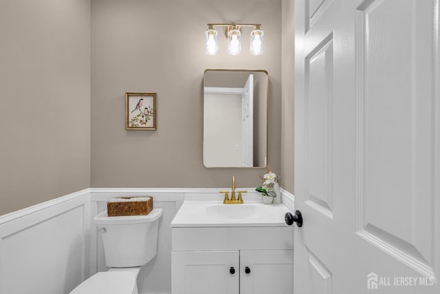 half bathroom featuring vanity, wainscoting, and toilet