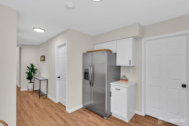 kitchen with stainless steel fridge, white cabinetry, light countertops, and light wood-style floors