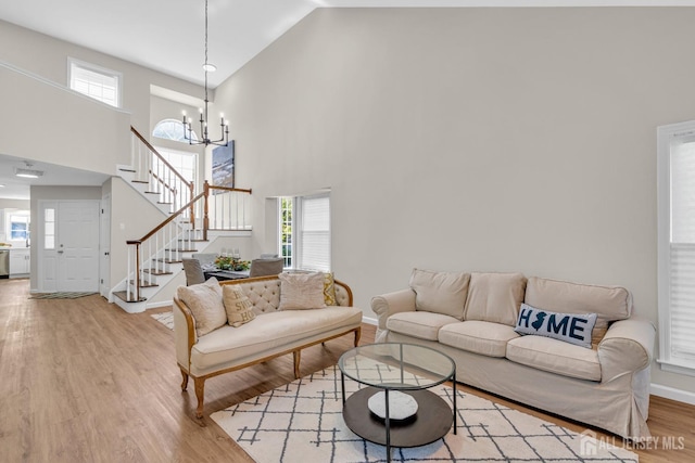 living room with a wealth of natural light, light wood-type flooring, a chandelier, and stairs