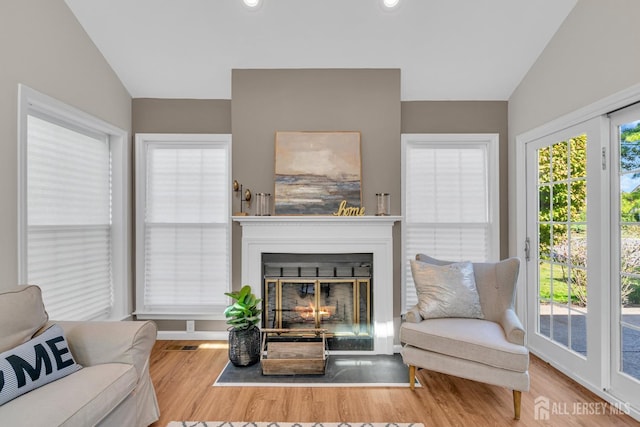 living area with a glass covered fireplace, lofted ceiling, and wood finished floors