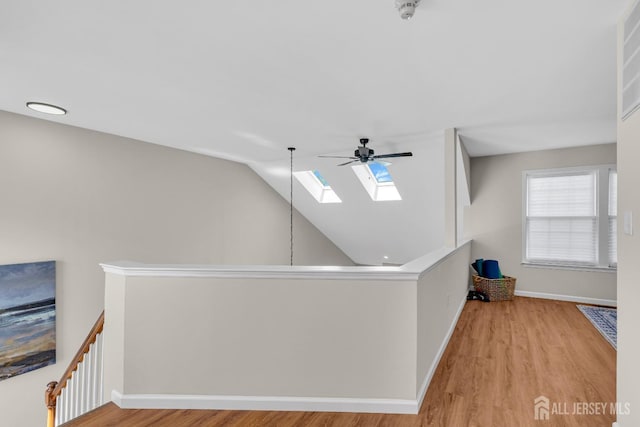 hallway with baseboards, an upstairs landing, wood finished floors, and vaulted ceiling with skylight