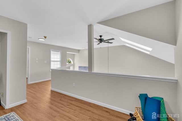 interior space featuring lofted ceiling with skylight, baseboards, ceiling fan, and wood finished floors