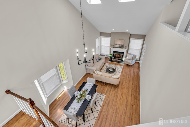 living area with a fireplace with flush hearth, light wood-style floors, a skylight, baseboards, and a chandelier