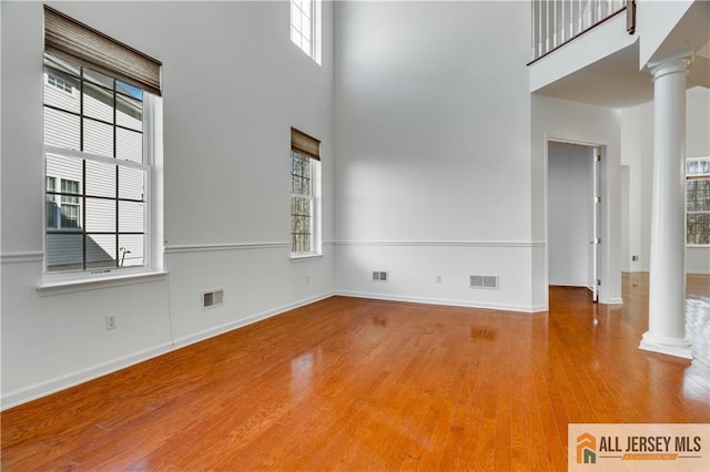 unfurnished living room featuring visible vents, a high ceiling, ornate columns, and wood finished floors