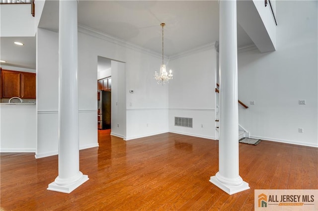 unfurnished dining area featuring stairs, crown molding, ornate columns, and wood finished floors