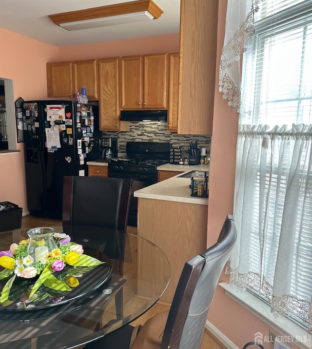 kitchen featuring under cabinet range hood, tasteful backsplash, black appliances, and light countertops