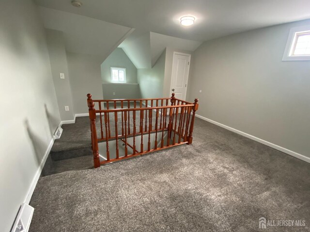 additional living space with dark colored carpet, plenty of natural light, and lofted ceiling