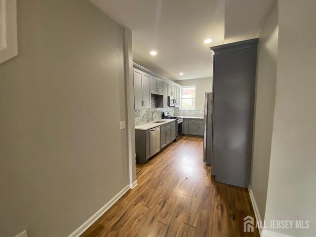 kitchen with appliances with stainless steel finishes, tasteful backsplash, gray cabinetry, sink, and wood-type flooring