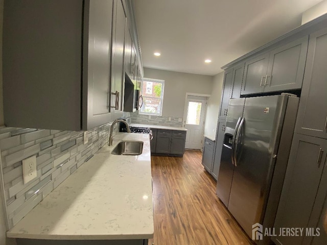 kitchen with gray cabinetry, light stone countertops, sink, tasteful backsplash, and stainless steel fridge with ice dispenser