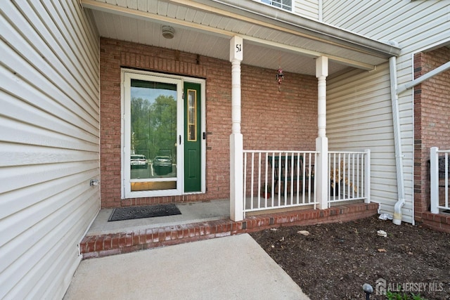 doorway to property featuring brick siding and covered porch