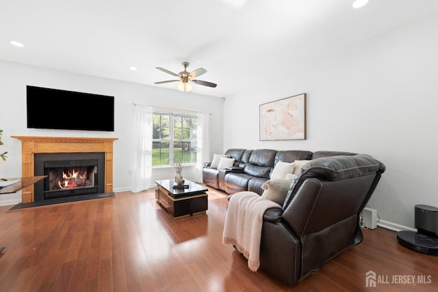 living room with wood finished floors, baseboards, ceiling fan, a warm lit fireplace, and recessed lighting