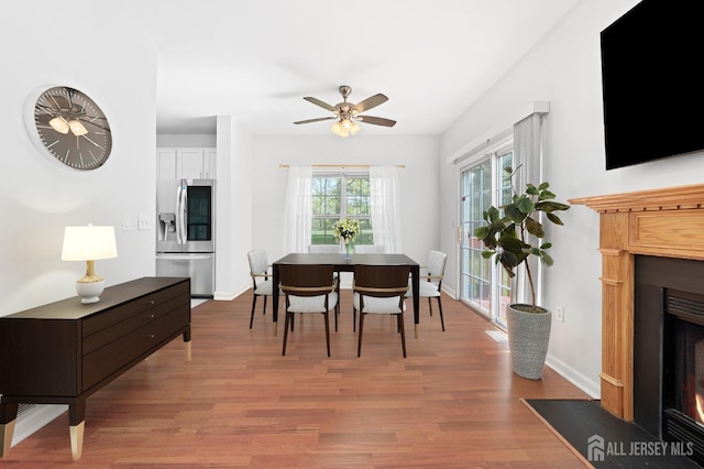 dining space featuring baseboards, a fireplace with flush hearth, ceiling fan, and wood finished floors