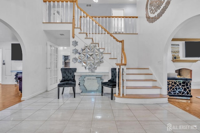 stairway with visible vents, baseboards, a high ceiling, a fireplace, and tile patterned floors