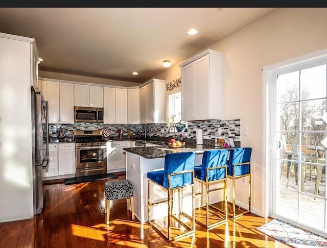 kitchen with white cabinetry, appliances with stainless steel finishes, a breakfast bar area, and dark stone counters