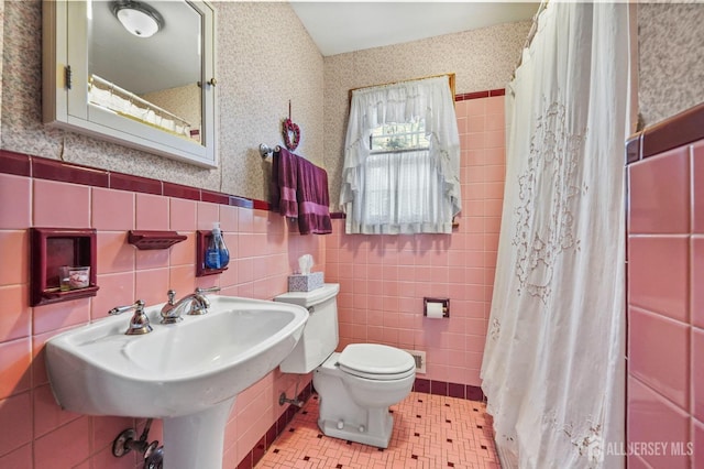 bathroom featuring wallpapered walls, wainscoting, toilet, tile patterned floors, and tile walls