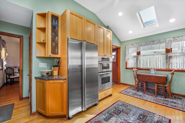 kitchen featuring stainless steel appliances, light wood-type flooring, lofted ceiling with skylight, dark countertops, and glass insert cabinets