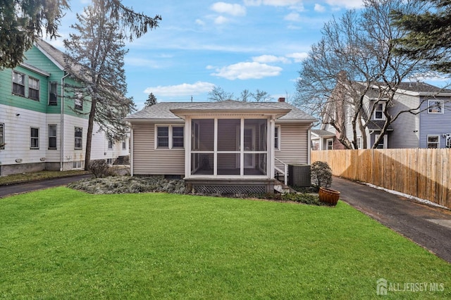 back of property with driveway, a lawn, a sunroom, a chimney, and fence