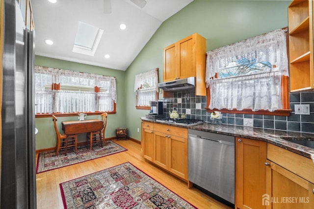 kitchen with vaulted ceiling with skylight, under cabinet range hood, stainless steel appliances, dark stone counters, and open shelves