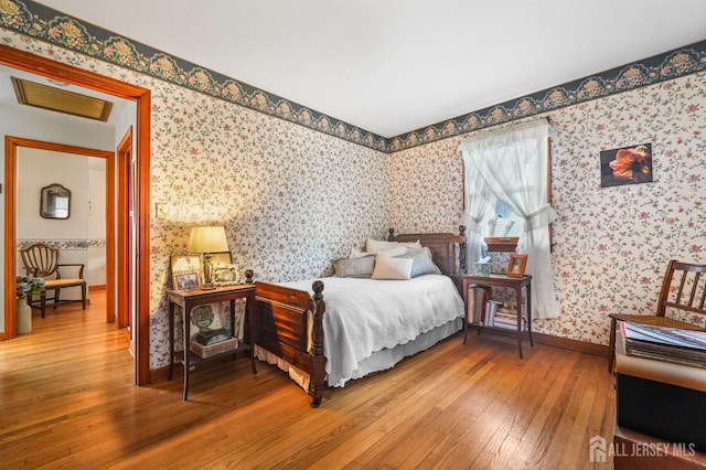 bedroom featuring baseboards, wood finished floors, and wallpapered walls