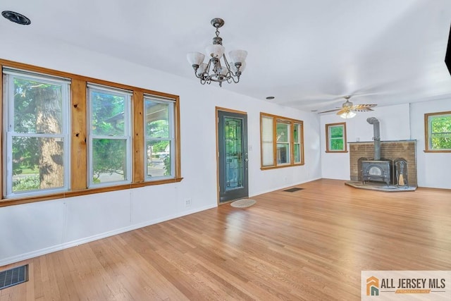 unfurnished living room with a wood stove, ceiling fan with notable chandelier, and light hardwood / wood-style floors