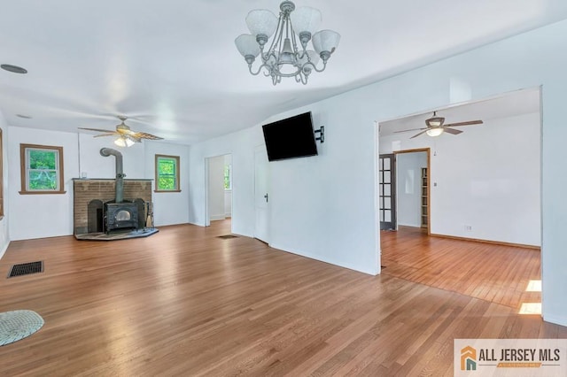 unfurnished living room featuring a healthy amount of sunlight, light wood-style floors, visible vents, and a wood stove