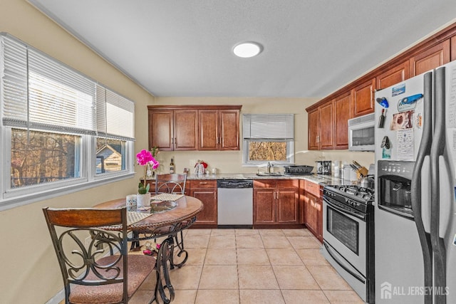 kitchen featuring stainless steel appliances, plenty of natural light, light tile patterned flooring, light stone counters, and sink