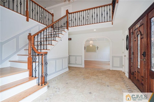 foyer featuring arched walkways, stone finish flooring, a decorative wall, and a towering ceiling