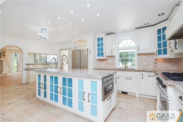 kitchen featuring premium appliances, a kitchen island with sink, decorative backsplash, and light stone countertops