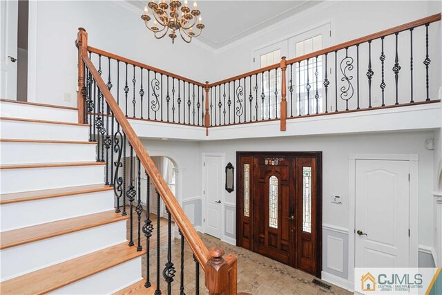 foyer entrance with visible vents, stairway, ornamental molding, a high ceiling, and a notable chandelier