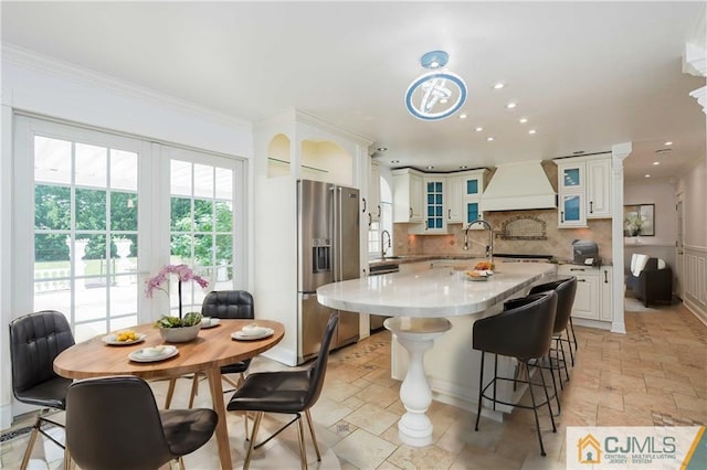 kitchen with stone tile floors, custom range hood, stainless steel refrigerator with ice dispenser, and backsplash