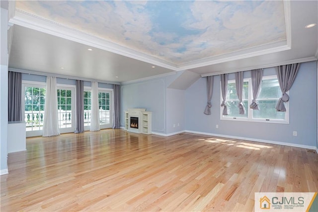 unfurnished living room with ornamental molding, a warm lit fireplace, plenty of natural light, and light wood finished floors