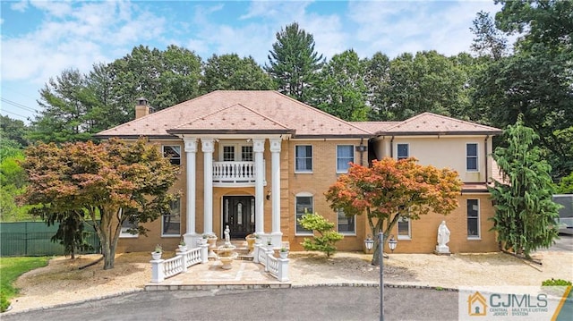 greek revival inspired property with a balcony, a chimney, and fence