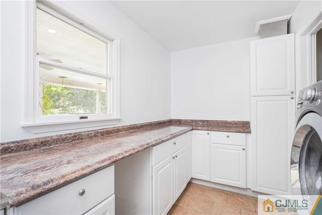 clothes washing area with stone finish floor, cabinet space, and washer / clothes dryer