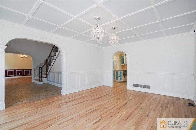 empty room with visible vents, arched walkways, stairway, wood finished floors, and an inviting chandelier