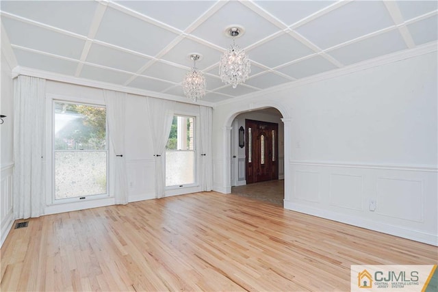 empty room featuring arched walkways, light wood-style flooring, coffered ceiling, visible vents, and an inviting chandelier