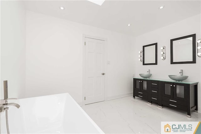 bathroom with marble finish floor, a freestanding bath, a sink, and recessed lighting