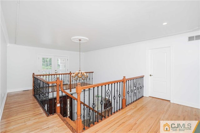 corridor featuring visible vents, ornamental molding, wood finished floors, and an upstairs landing