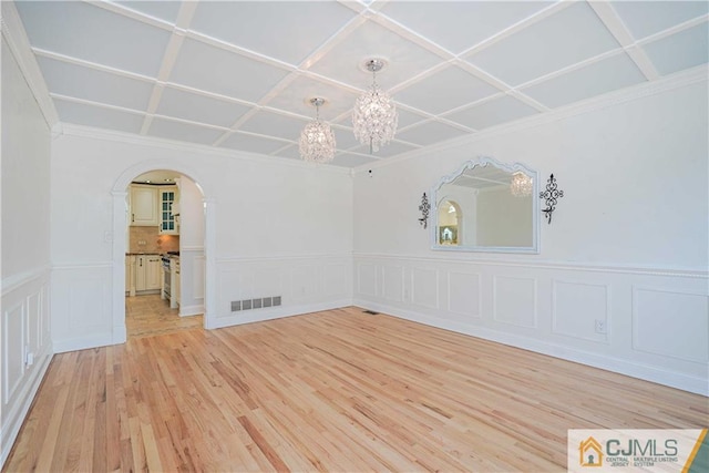 empty room with arched walkways, visible vents, an inviting chandelier, light wood-style floors, and coffered ceiling