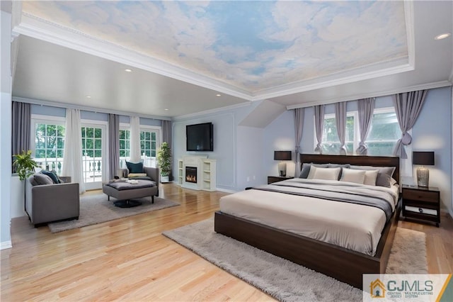 bedroom featuring wood finished floors, a lit fireplace, access to outside, a tray ceiling, and crown molding