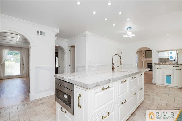 kitchen featuring arched walkways, visible vents, stainless steel microwave, and a sink