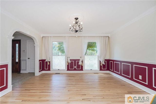 interior space with light wood finished floors, arched walkways, a wainscoted wall, an inviting chandelier, and crown molding