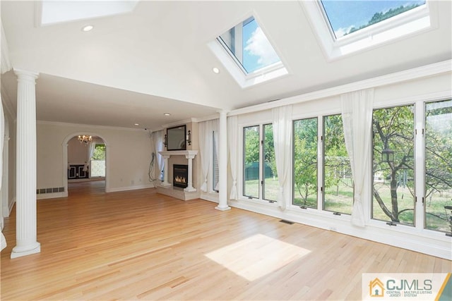 unfurnished living room with ornamental molding, a wealth of natural light, a warm lit fireplace, and decorative columns