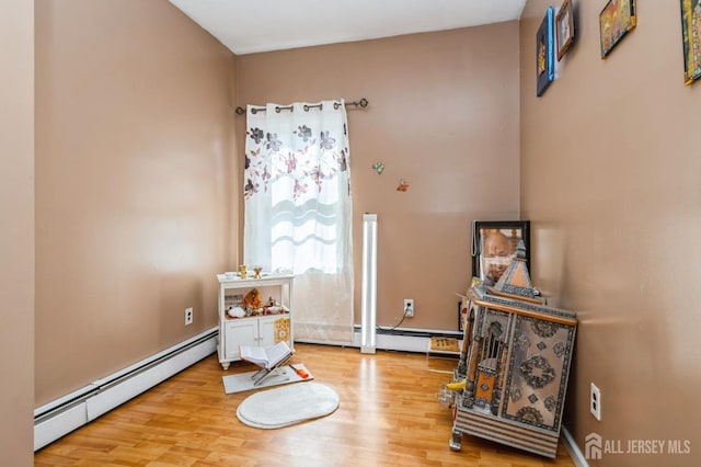 living area featuring wood finished floors, a wood stove, and a baseboard radiator