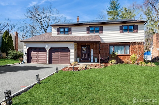 traditional home with brick siding, a chimney, a front yard, roof mounted solar panels, and driveway