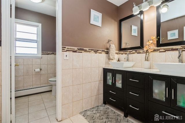 full bathroom with double vanity, tile patterned flooring, a baseboard heating unit, and a sink