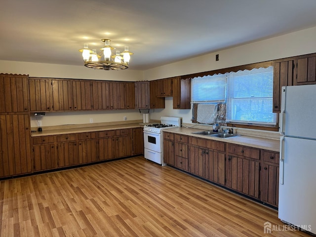 kitchen featuring light wood-style flooring, a sink, white appliances, light countertops, and a chandelier