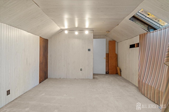 bonus room with lofted ceiling with skylight, wooden walls, and light carpet