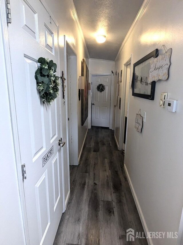 corridor with dark wood-type flooring, a textured ceiling, and crown molding