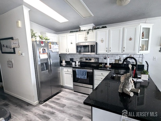 kitchen with light wood finished floors, stainless steel appliances, decorative backsplash, white cabinets, and a sink