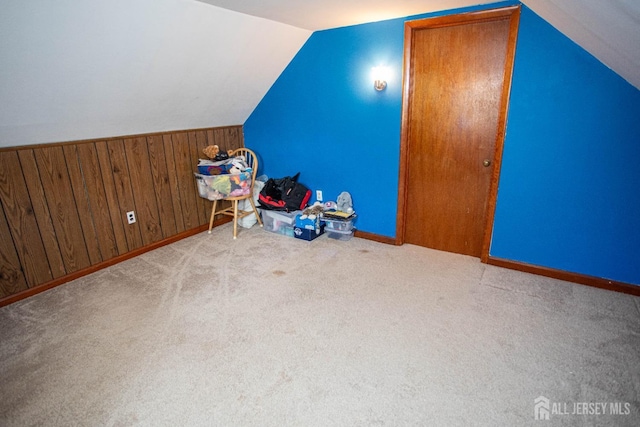 additional living space featuring light carpet, lofted ceiling, and wood walls